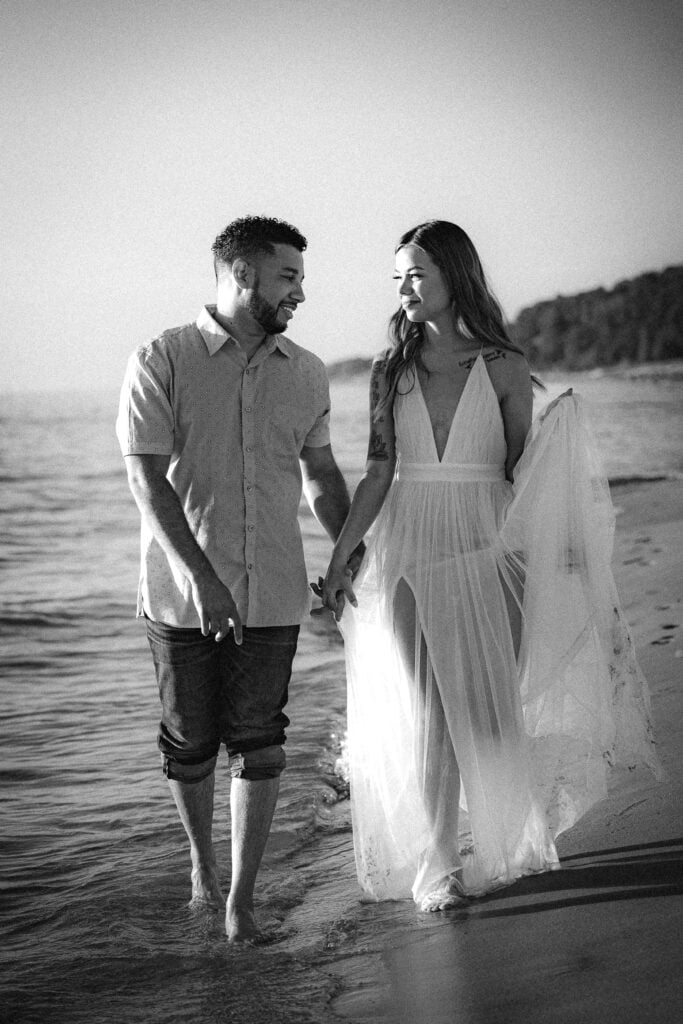 Black and white image of a couple walking hand in hand down a beach during their elopement.