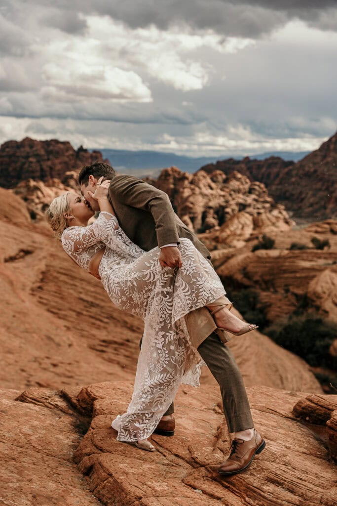 Groom dips bride for a kiss while they stand on Red Rocks in Utah.