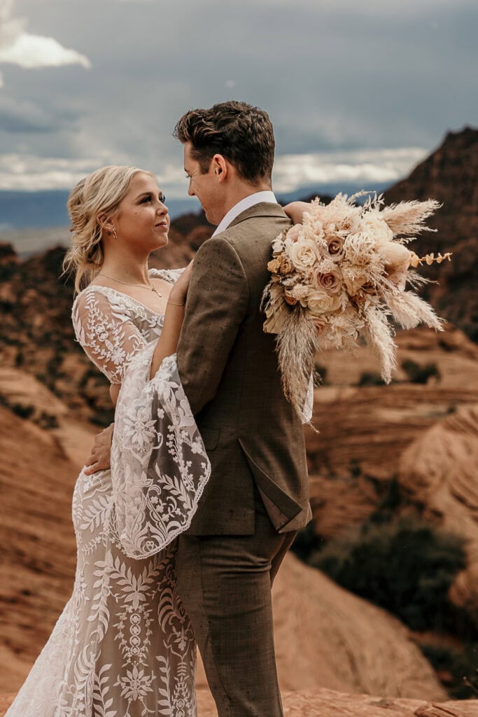 Bride and groom look at each other in front of red rocks.