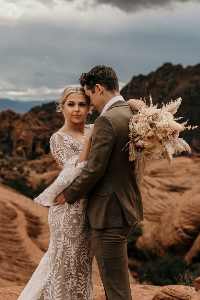 Boho styled bride and groom pose for photo on top of red rocks in Utah desert.