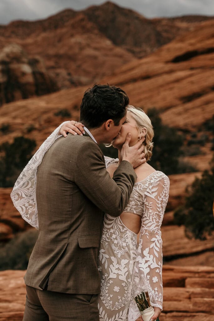 Boho bride and groom kiss passionately on Utah red rocks.