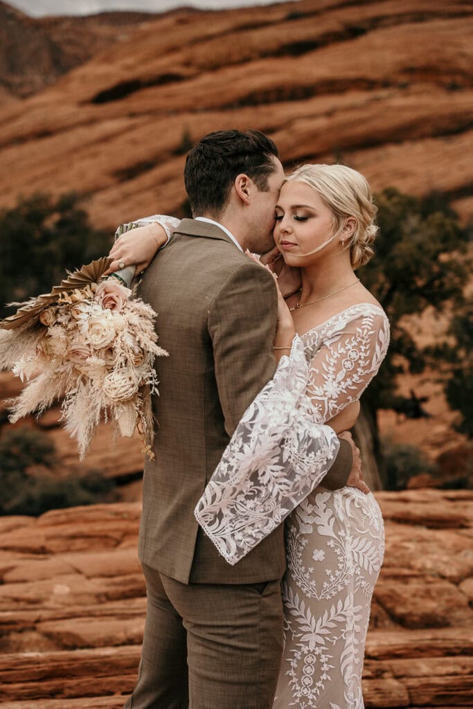 Bride and groom embrace while standing in the desert.