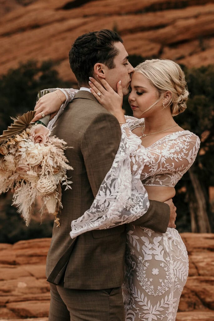 Groom kisses the bride on the forehead as she tenderly touches his face.