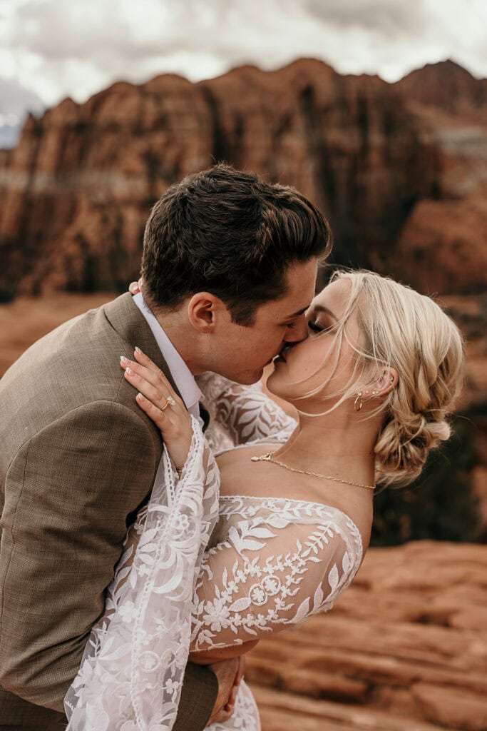 Groom dip kisses his bride in front of giant rock formations in the desert.