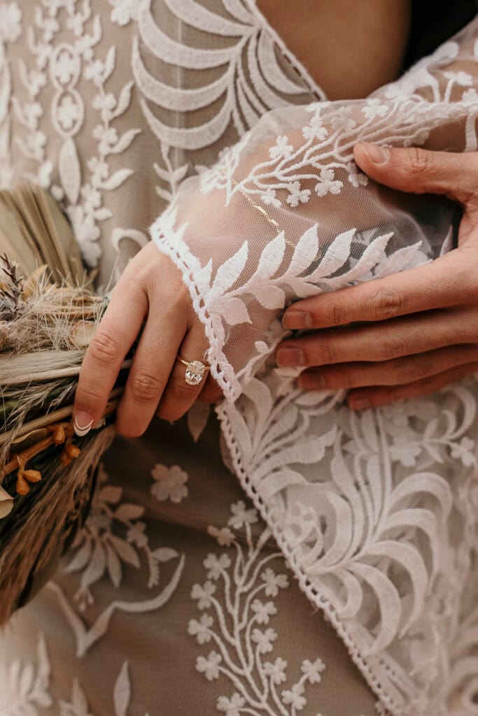 Groom touches bride's arm while she hold her bouquet to show off her wedding ring.