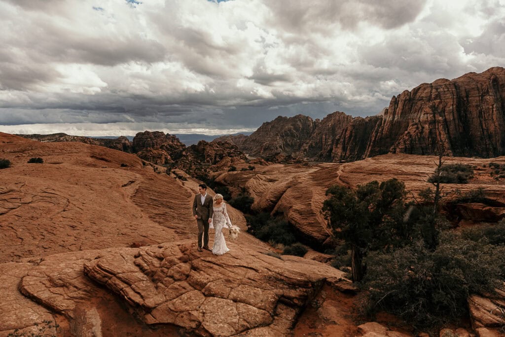 A boho bride and groom stand on sand dunes in the Utah desert.