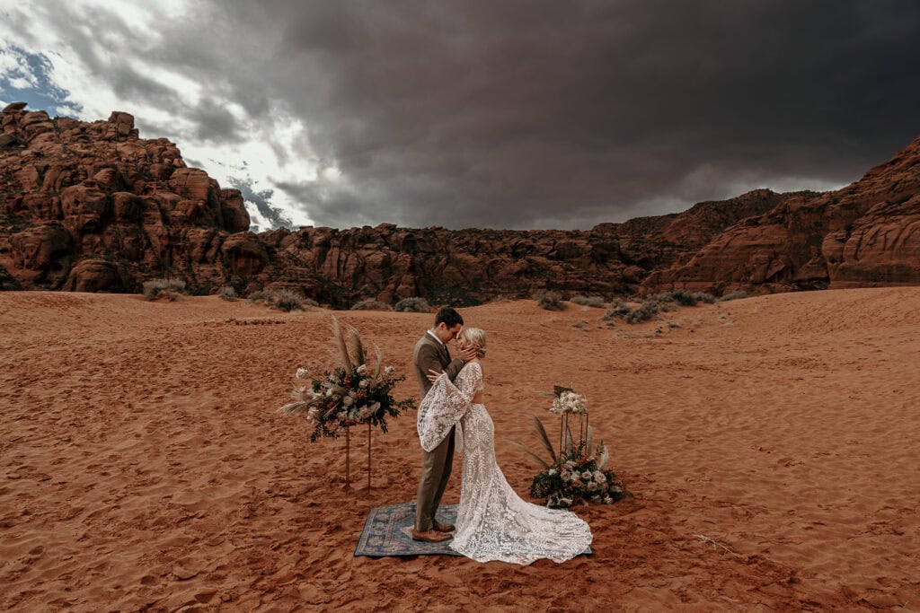 A couple elopes on sand dunes in Utah while a storm rolls in behind them.