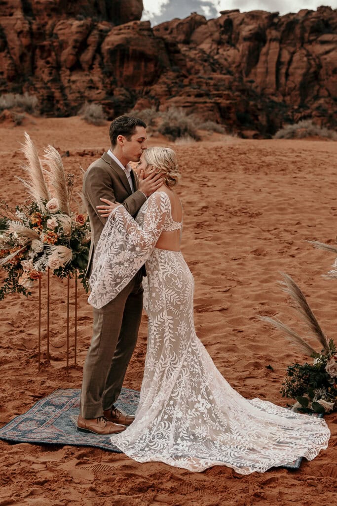 A couple elopes on a bohemian rug on sand dunes in Utah.