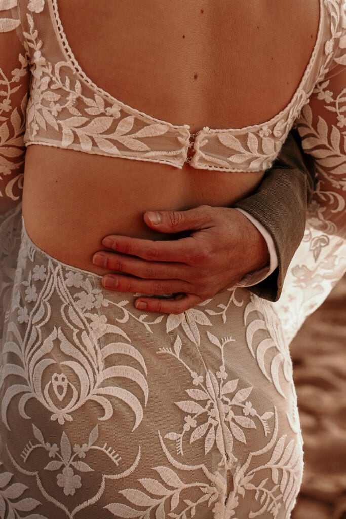 Closeup of a groom's hand on the bride's back.