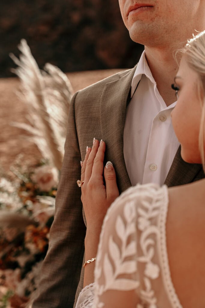 Closeup of the bride's hand on groom's chest during their wedding ceremony.