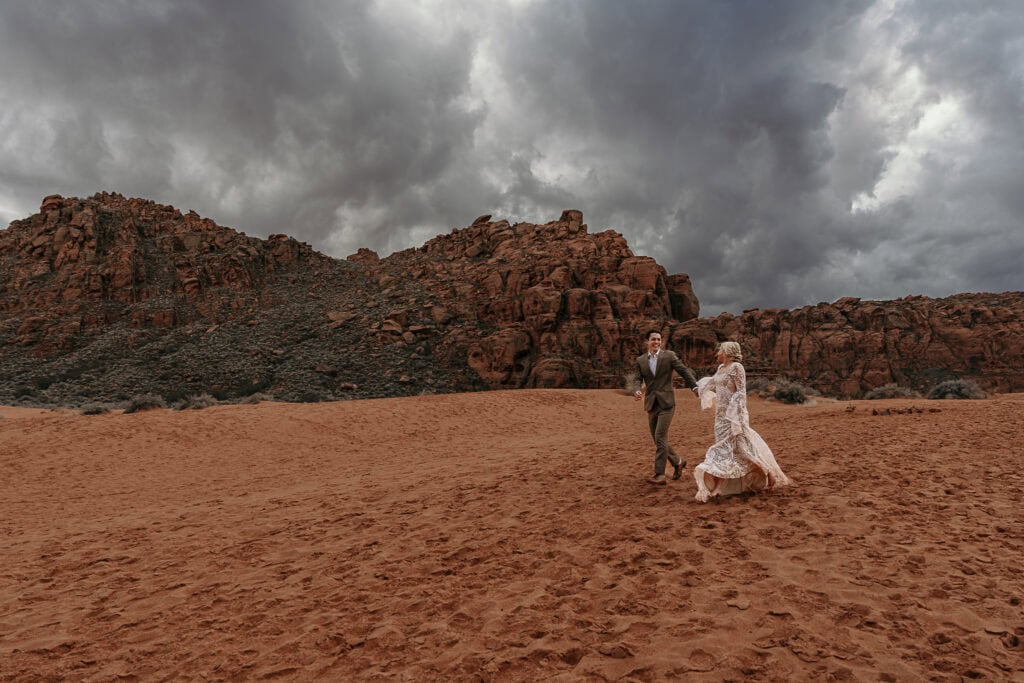 Bride and groom playfully run on the sand dunes in Utah.