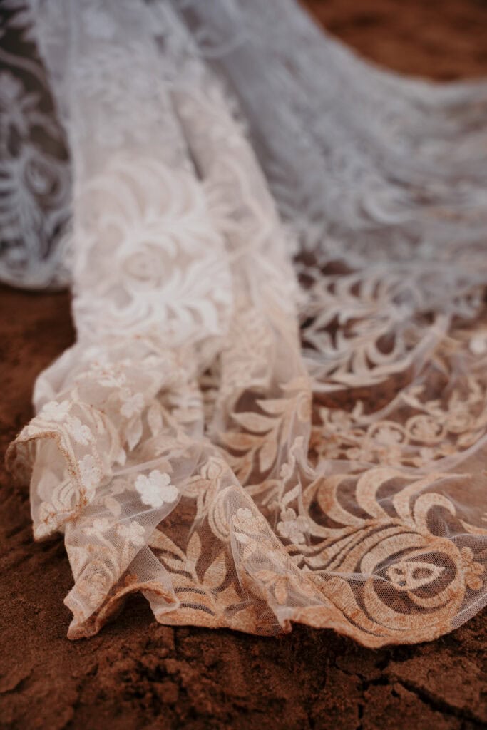 A lacy wedding gown hem on red sand.