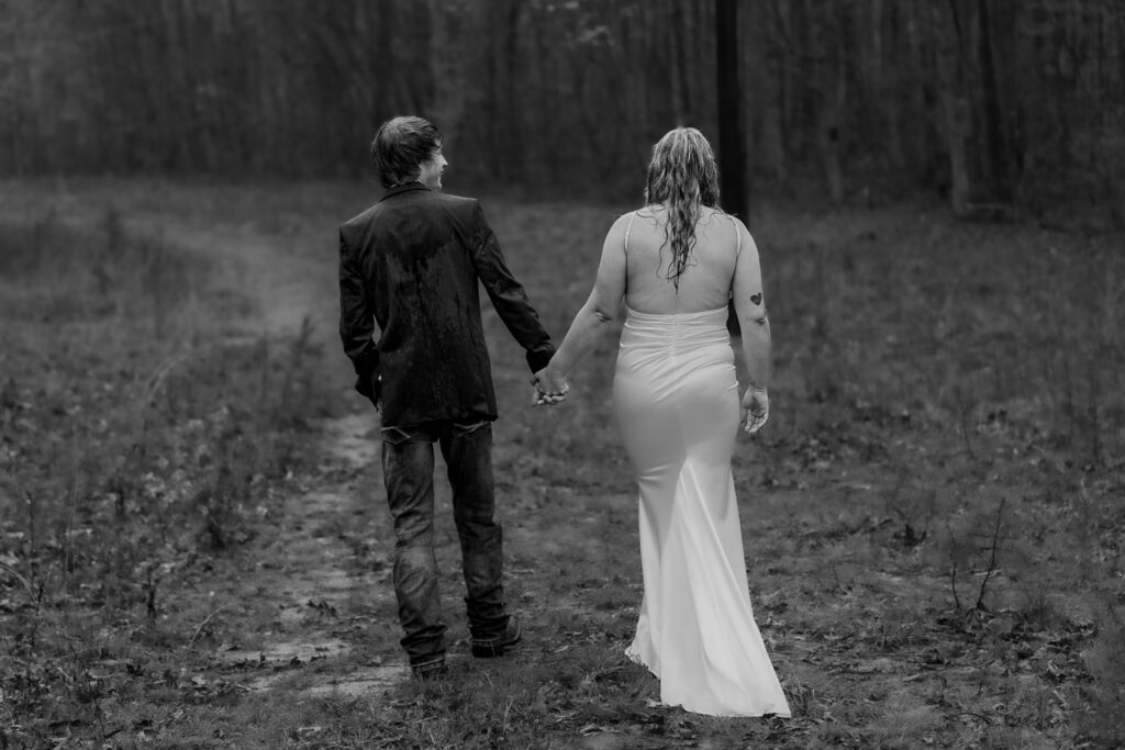 Black and white image of a couple walking in the rain down a muddle trail.