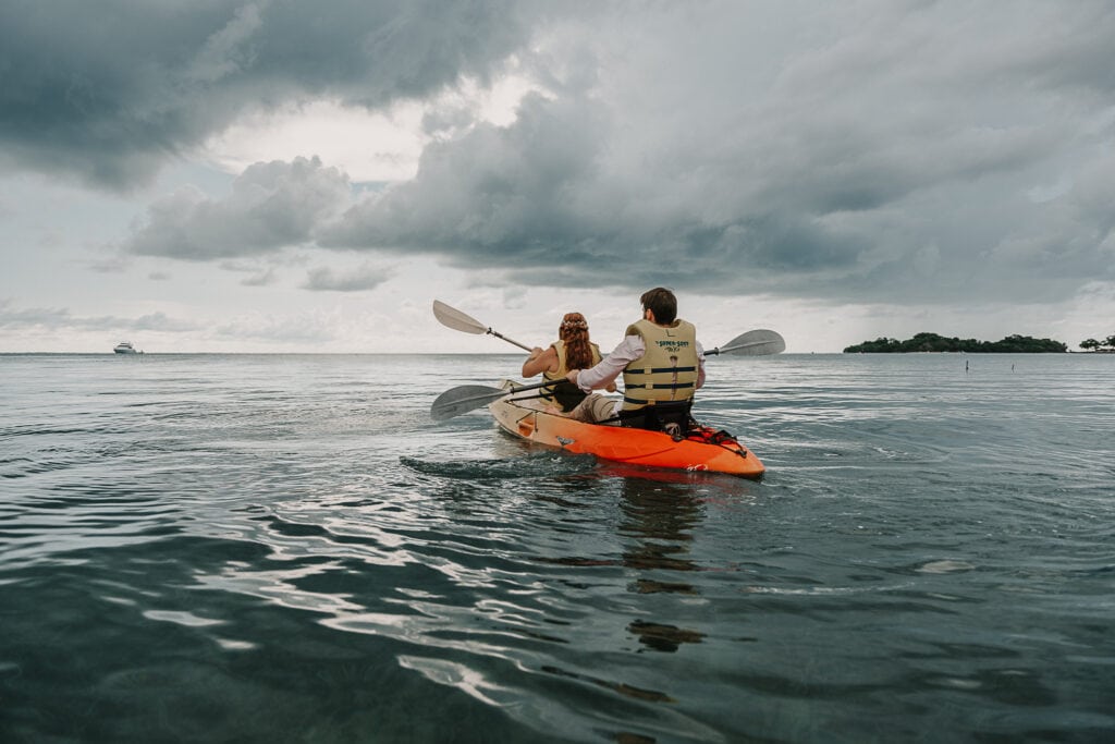 A couple in wedding attire kayaks in the Caribbean during their Jamaican elopement.