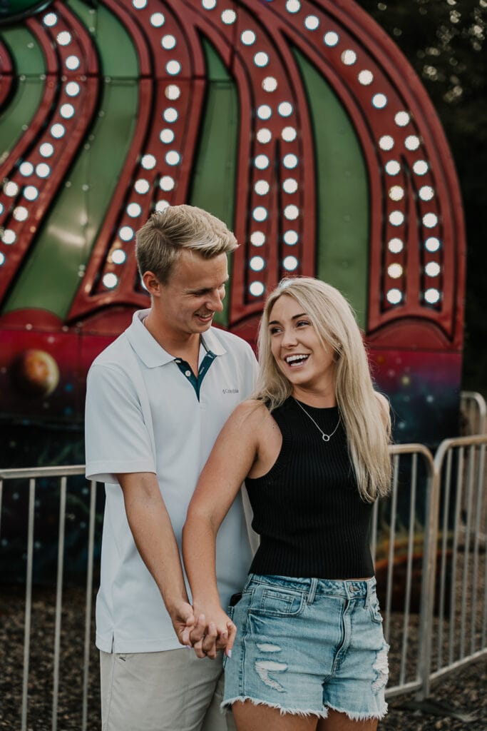 Mattison and Jordan hold hands, looking at each other in front of the lights of a fair ride.