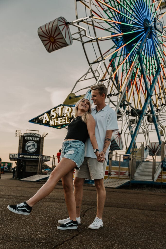 Couple playfully holds hands while looking at each other in front of the Ferris wheel.