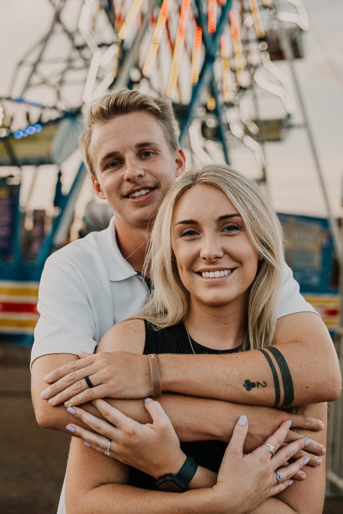 Engaged couple stands in front of the Ferris wheel.