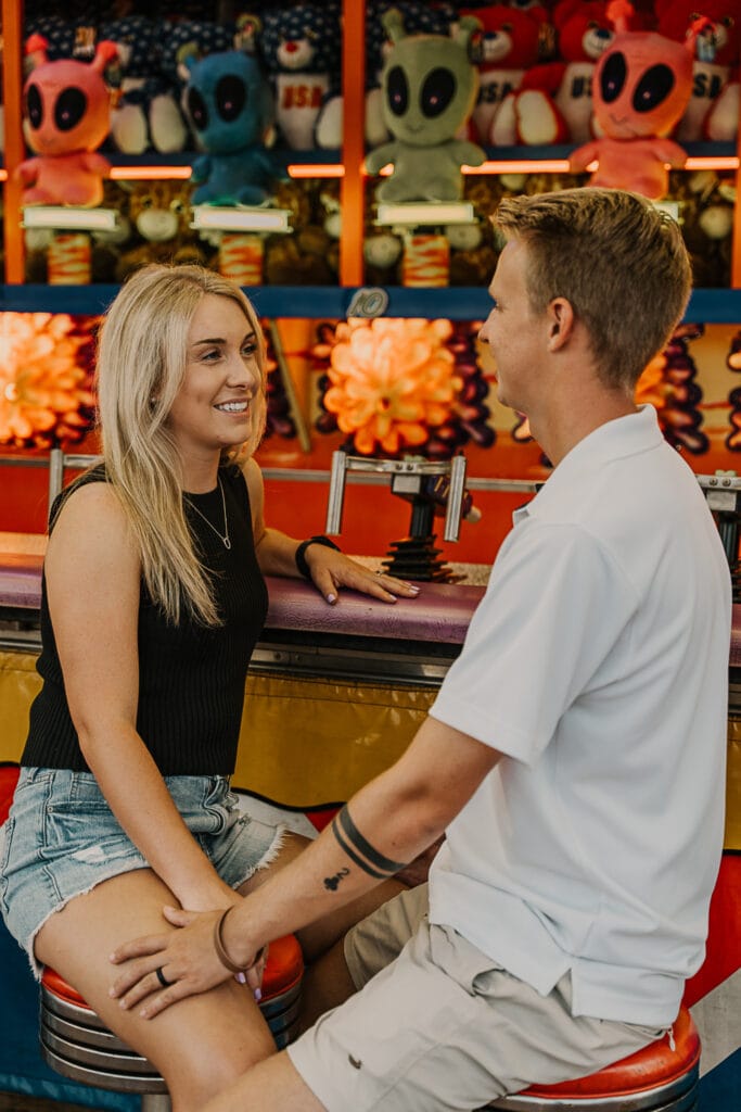 Mattison & Jordan talk while sit in front of a game at the fair, facing each other.