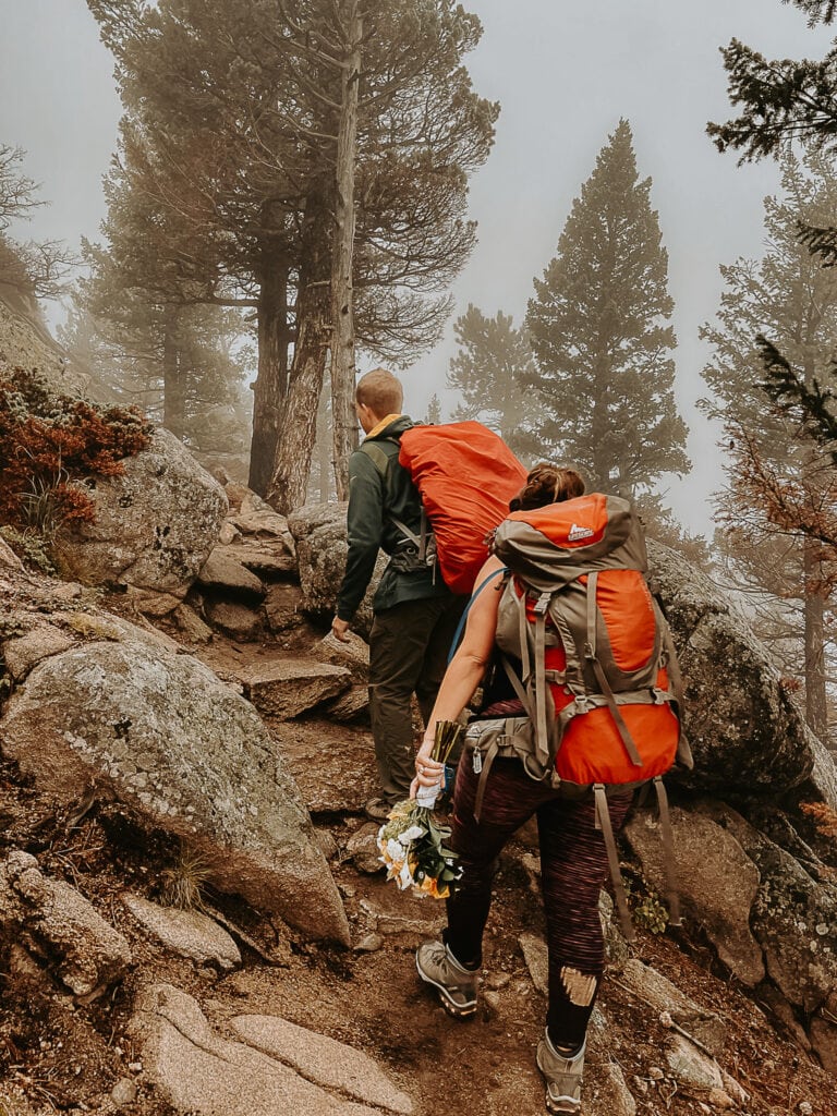 Couple hikes up trail in Estes Park CO for their elopement. Bride is carrying her bouquet.