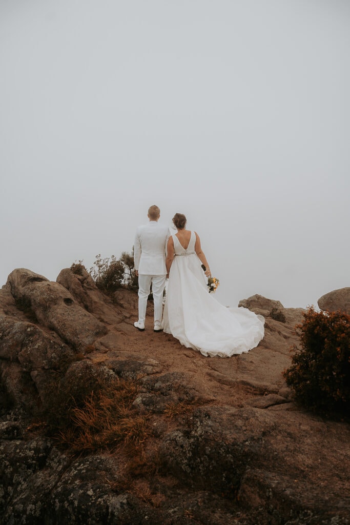 Bride & Groom stand side by side on the top of Kruger Rock. The background is very foggy and you cannot see Estes Park,
