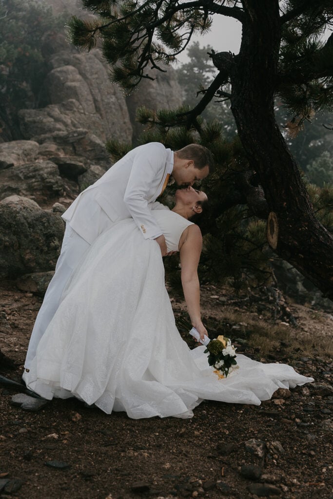 Groom dips bride for a kiss during the Colorado elopement ceremony on Kruger Rock on a foggy day.