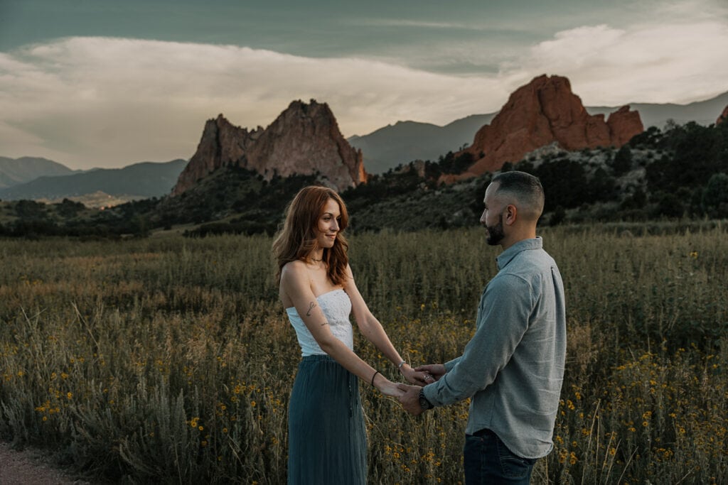 Couple holds both hands and face each other smiling while standing in Garden of the Gods, CO.