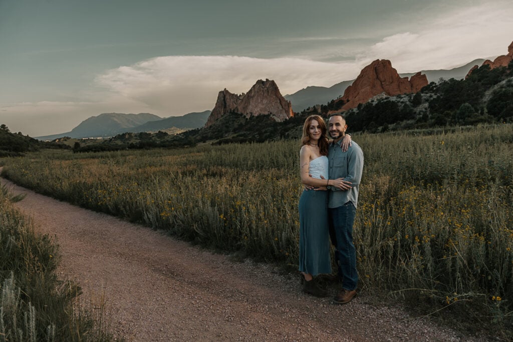 Couple stands on a trail in Garden of the Gods. Wildflowers and rock formations are in the background.