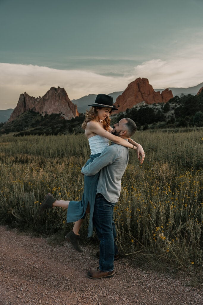 Couple stands in the middle of the trail in Garden of the Gods and holds hands while kissing.