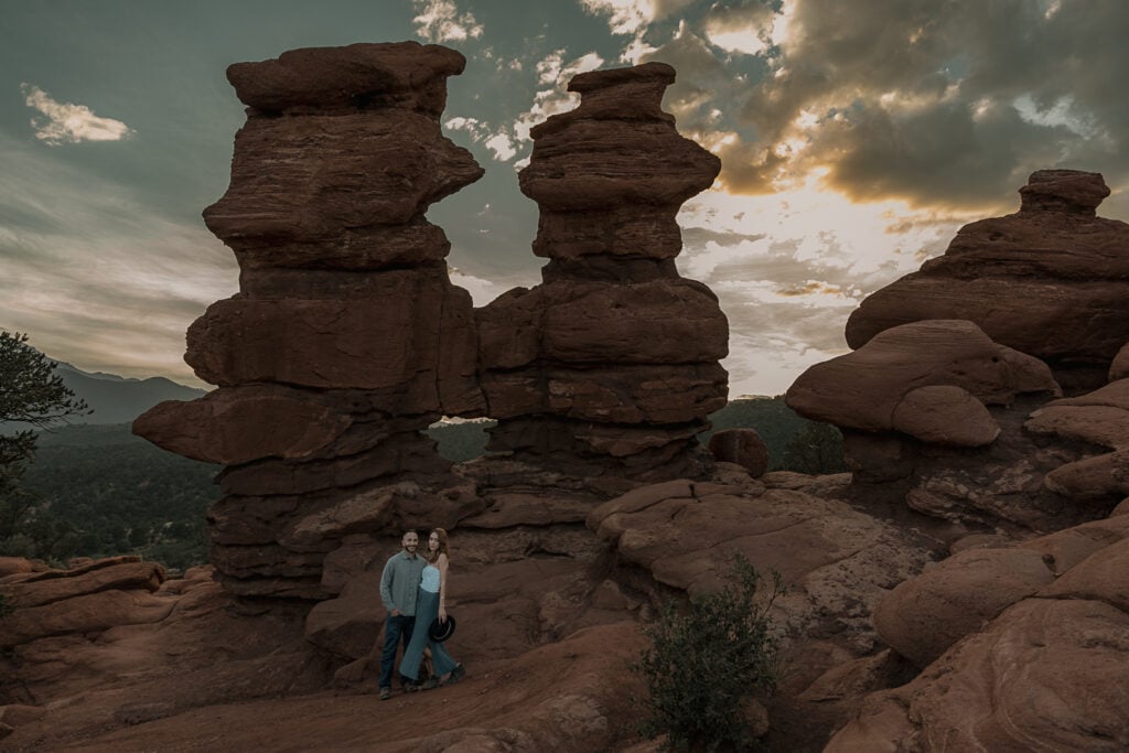 Couple stands in front of Siamese twins rock formation during sunset. They are wearing denim outfits.