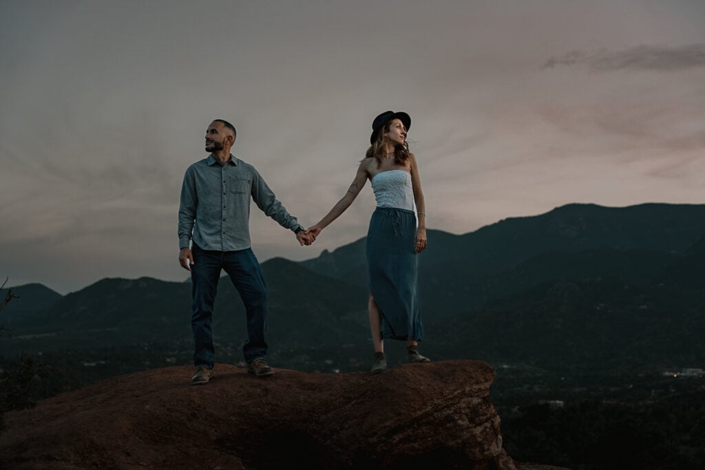 Couple in denim stand hand in hand while facing opposite directions on top of cliff in Garden of the Gods.