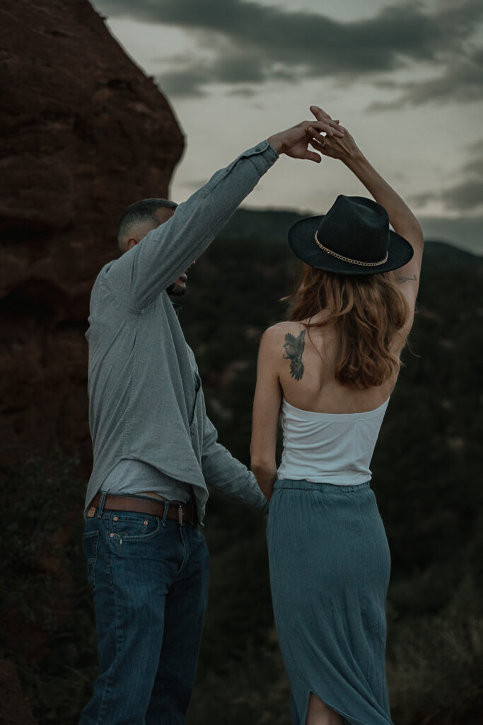 Man spins woman as they dance at sunset in front of the mountains in Colorado.