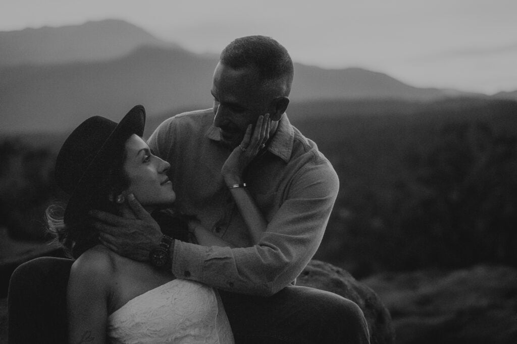 Romantic black and white image of couple in front of mountains. They are both touching each other's face.