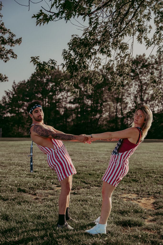 Michelle and Alex, in matching overalls, hold hands and lean back away from each other.