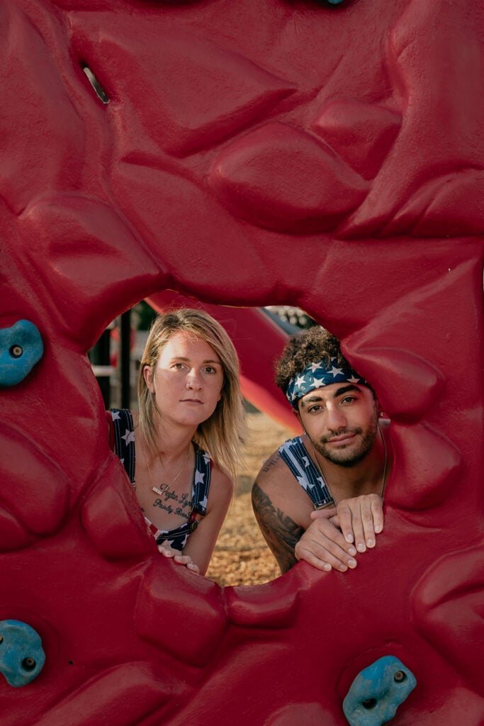 Couple peeks through rock wall on playground during their Masterminds photoshoot.