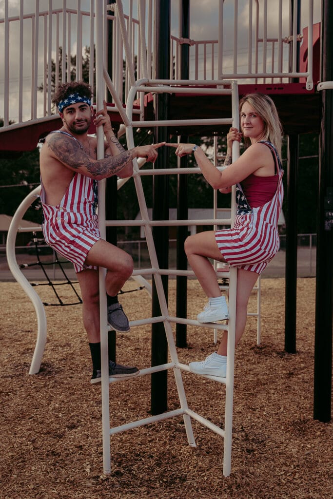 Couple climbs up ladder in playground during their silly Masterminds photoshoot.