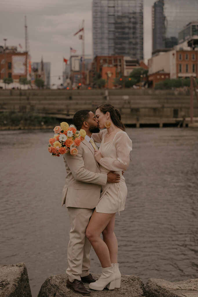 Couple kisses after wedding ceremony in Cumberland Park. Downtown Nashville & the Cumberland River are behind them