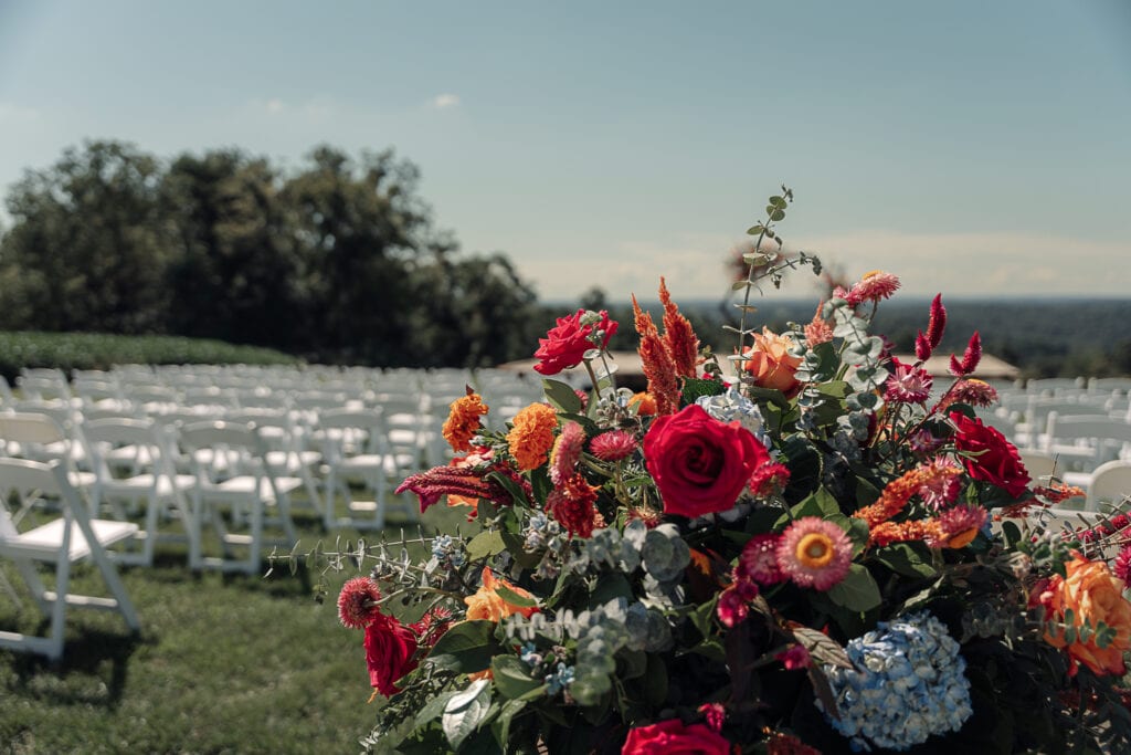 A beautiful brightly colored bouquet sits behind white folding chairs that are set up for an outdoor ceremony.