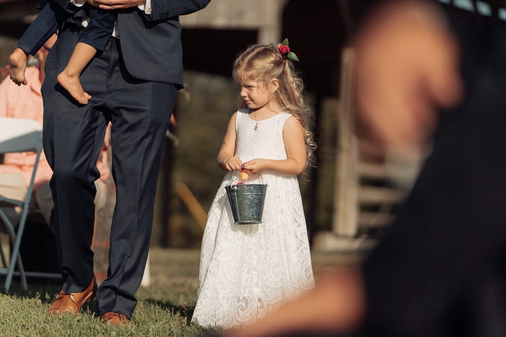 A flower girl walks down the aisle with a little metal bucket full of petals.
