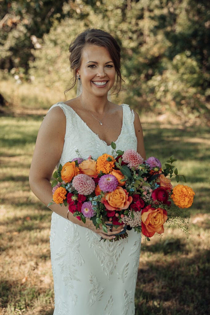 Bride holds a beautiful bright bouquet of flowers as she stands outside.