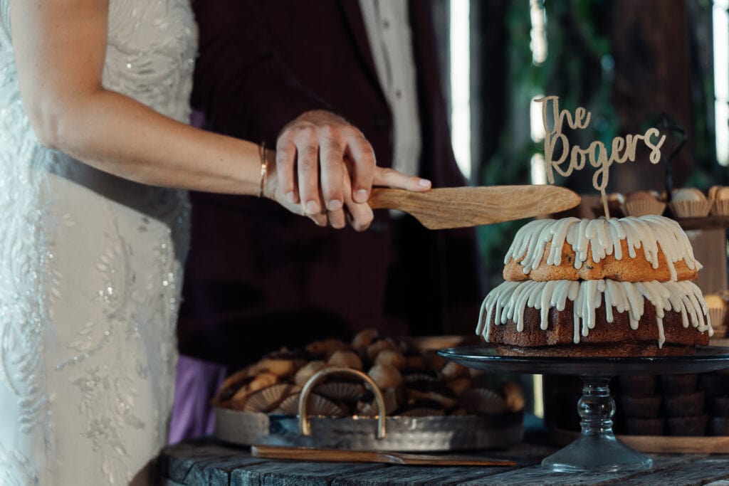 Closeup of bride & groom cutting their bundt cake with a wooden knife at their reception.
