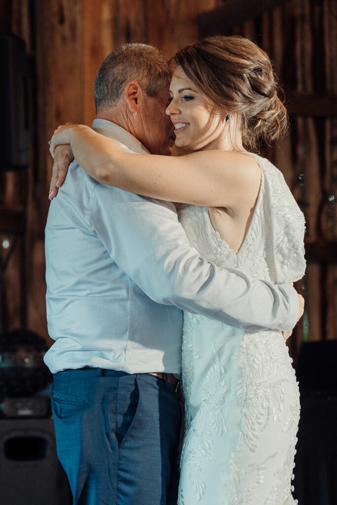 A bride dances with her dad at her wedding reception in a barn.