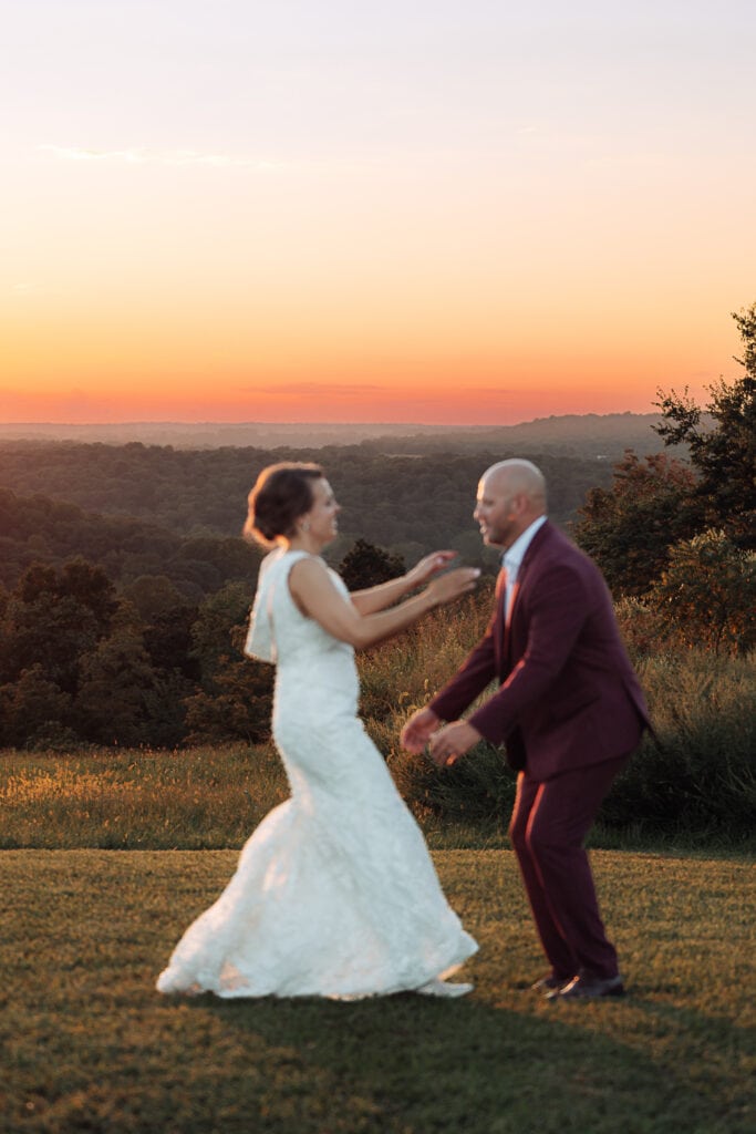 A woman run towards the groom, who is going to lift her up and spin her. The sunset behind them is in focus. The couple is out of focus.