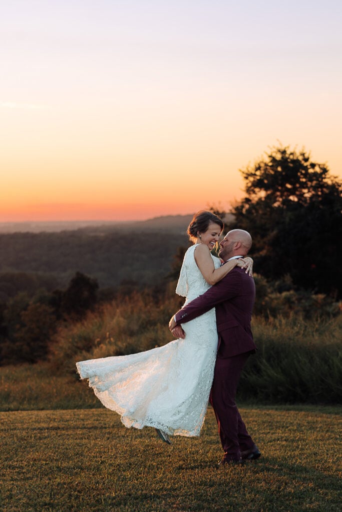 A groom spins the bride around outside during sunset, as they look at each other and laugh.