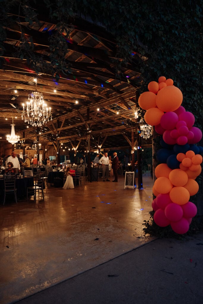 A colorful balloon arch frames a rustic barn for a wedding reception.