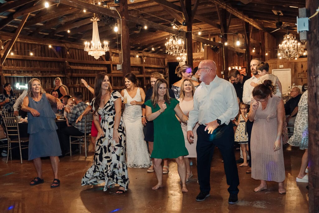 The dance floor at a barn reception is full of guests dancing and laughing together.