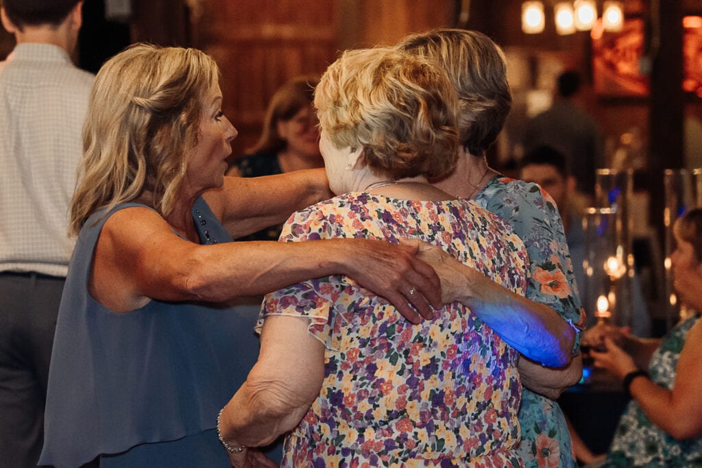 A group of women dance with their arms around each other during a reception.