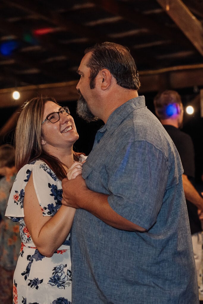 A man and woman dance during a wedding reception as she looks up at him and laughs.