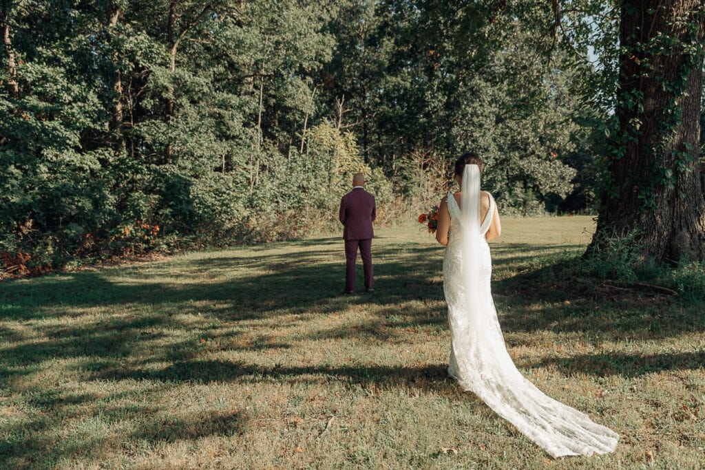 Bride walks up behind the groom outdoors for a first look before their wedding.