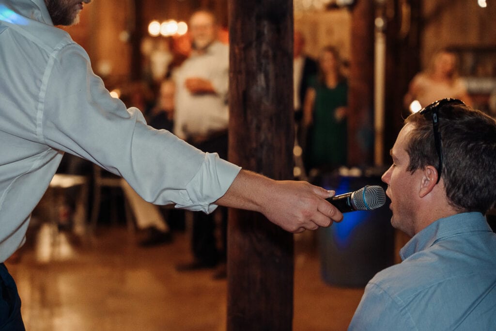 A man holds a microphone up to another man's mouth during a wedding reception.