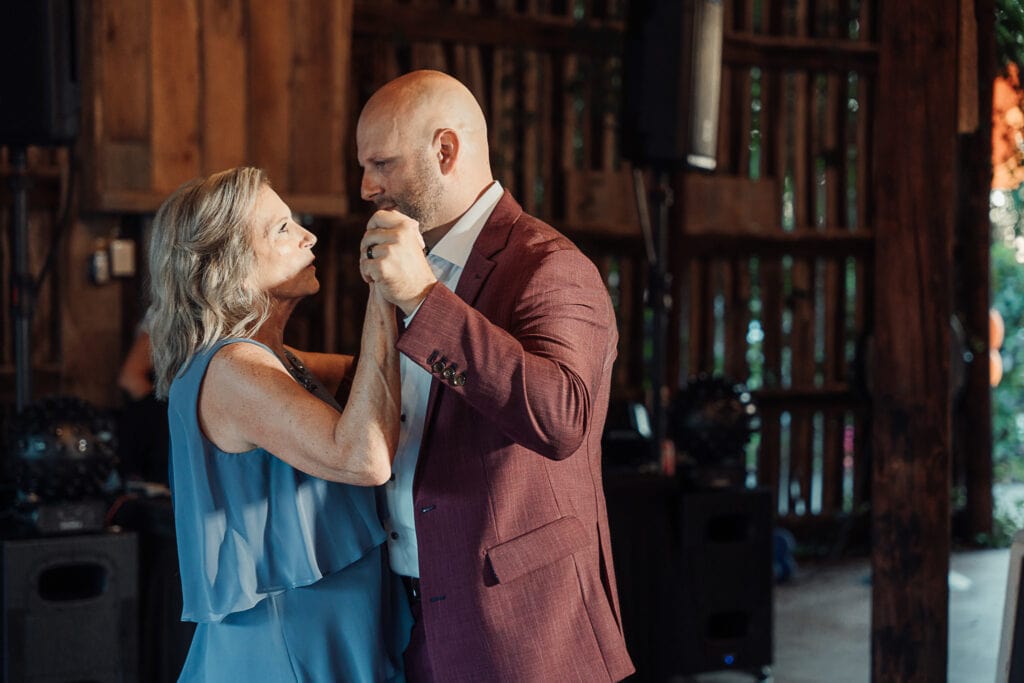 AJ dances with his mom during his wedding reception. They're in a rustic barn.